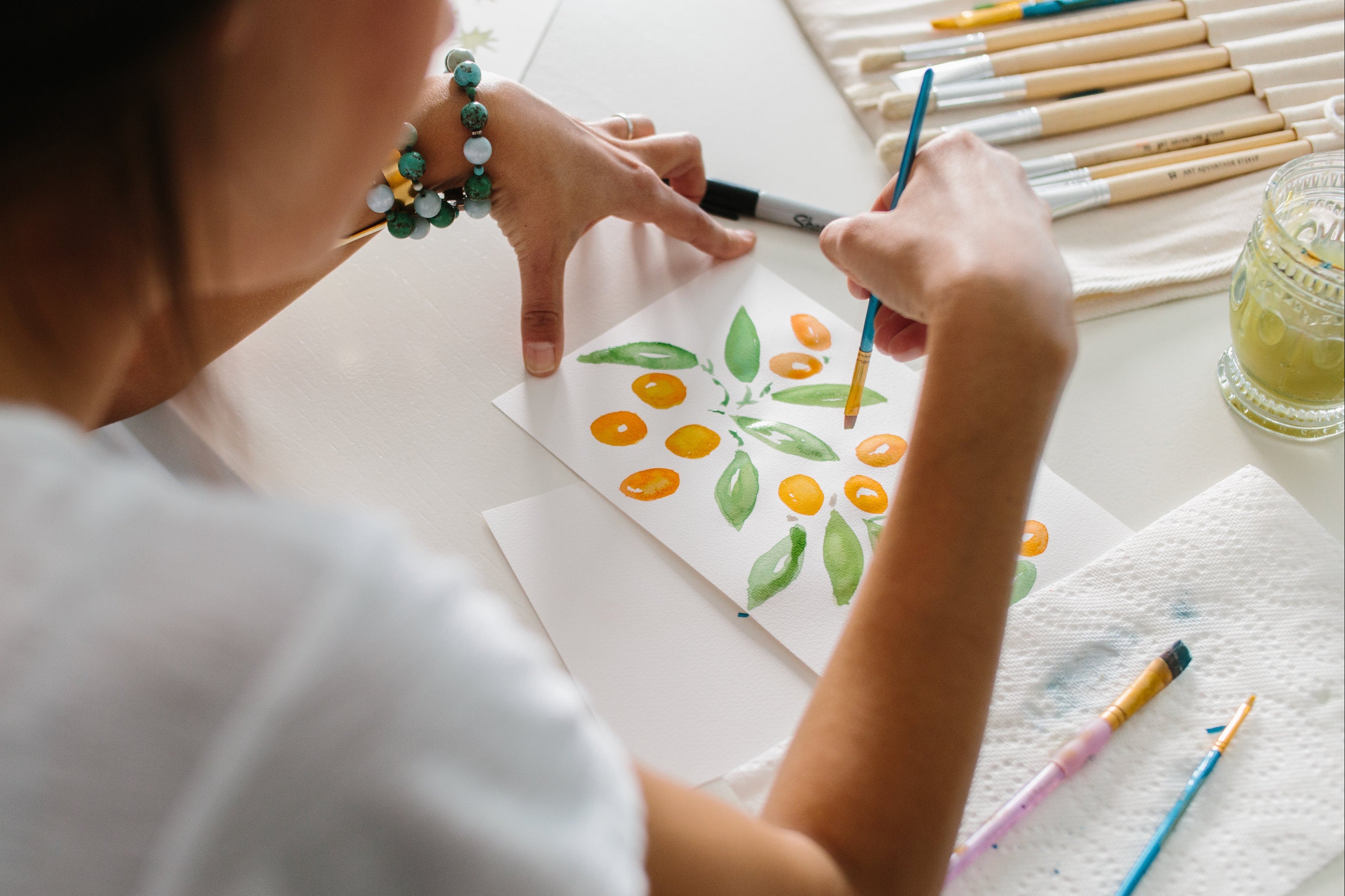 Person painting a watercolor design on paper with brushes and paint.